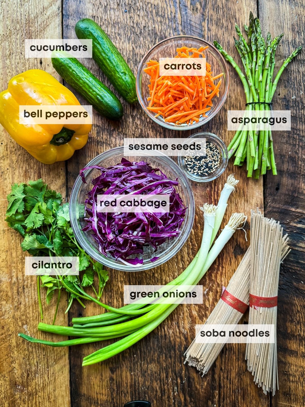 Labeled ingredients for making a vibrant Vegan Asian Noodle Salad on top of a wooden board.