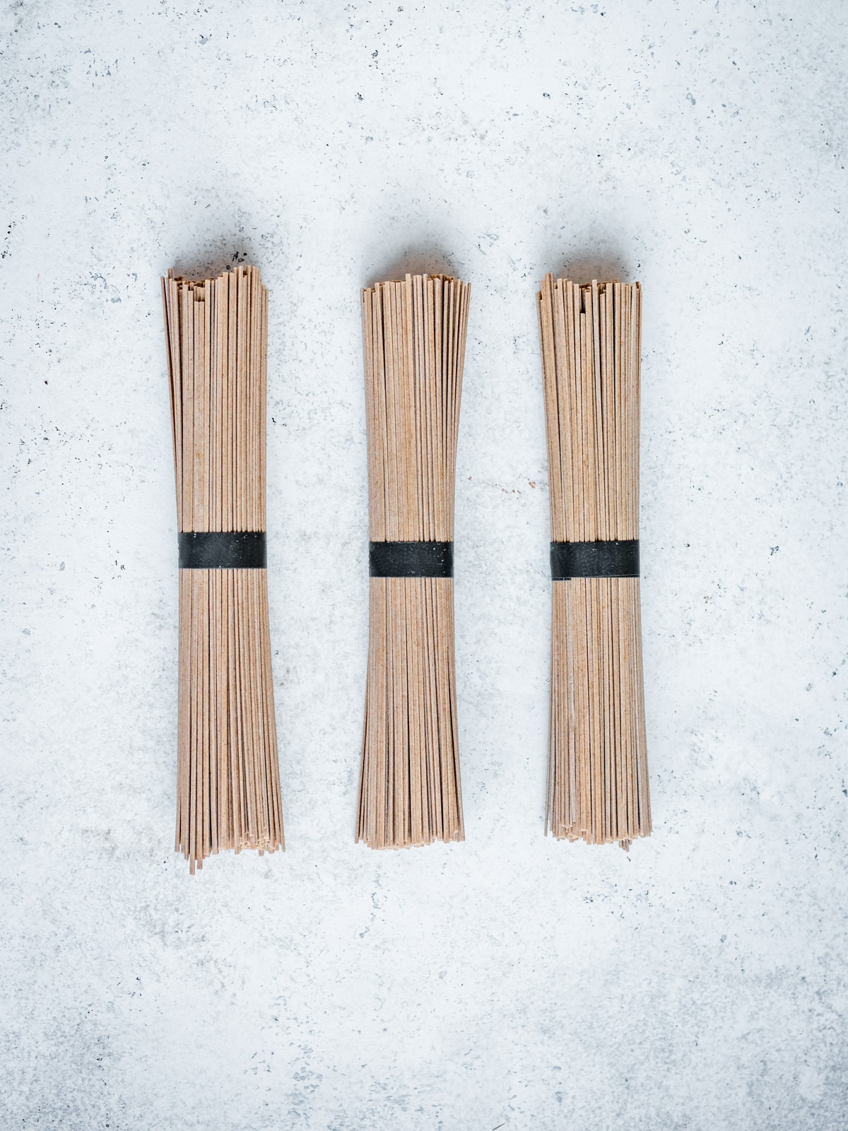 Three bundles of dried buckwheat soba noodles on top of a white concrete surface.