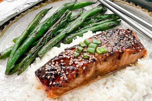 A filet of broiled miso glazed salmon on top of white rice with blistered green beans on the side.