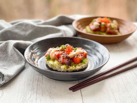 Sushi waffles with salmon and tuna on two round plates with a side of chopsticks on top of a white surface with a napkin in the background.