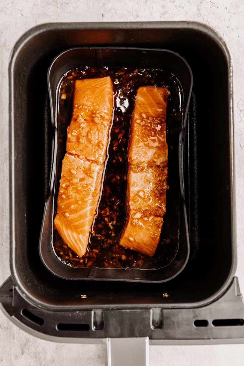 Two raw salmon filets in sauce placed in an air fryer.