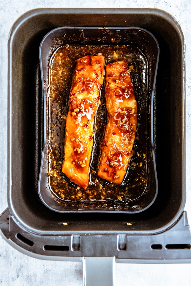 Cooked salmon filets topped with teriyaki sauce in an air fryer.